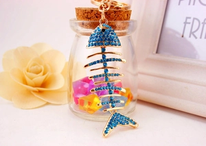 Detailed macro of gold-plated fishbone keychain with blue crystals on a glass bottle