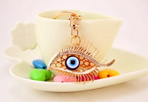 Close-up of golden evil eye keychain with rhinestones and lashes on a coffee cup