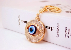 Detail of golden Evil Eye keychain with sparkling crystals on a decorative book background