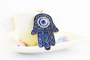 Detailed view of Hamsa Hand pendant with blue enamel, evil eye, and crystal inlay