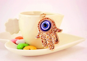 Detail der Hamsa-Hand Schlüsselanhänger mit bösem Blick und Strass auf Kaffeetassen-Hintergrund