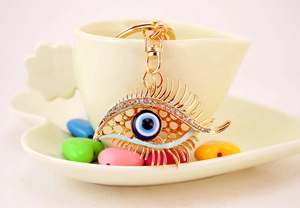 Macro detail of Evil Eye keychain with long eyelashes and rhinestones on a ceramic cup
