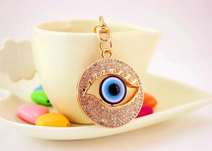 Detail shot of a golden Evil Eye keychain with sparkling rhinestones on a coffee cup