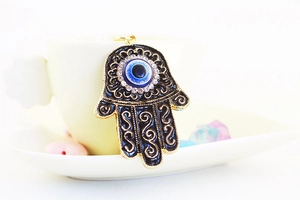 Macro detail of Hamsa pendant with black enamel dripping oil and blue evil eye charm