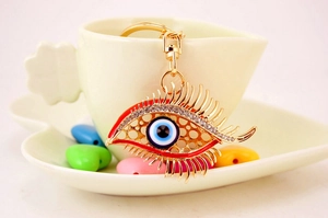 Detail of evil eye keychain featuring gold eyelashes, rhinestones, and blue enamel charms