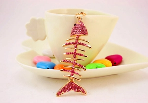 Detail of rose gold fish bone keychain with pink crystals hanging on a cup edge