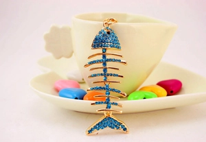 Detail view of a creative fish bone keychain with blue crystals on a golden metal base