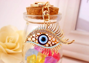 Macro shot of gold-plated evil eye keychain with rhinestones and long lashes by glass bottle