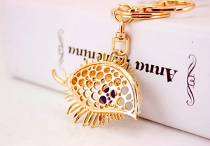 Macro shot of gold evil eye keychain with blue bead and eyelash detail on white book