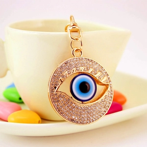 Sparkling Evil Eye keychain with blue rhinestones hanging on a cream ceramic cup edge