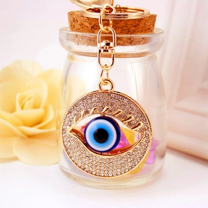Golden Evil Eye keychain with sparkling crystals hanging on a glass bottle display