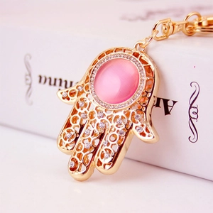 Goldener Hamsa-Hand Schlüsselanhänger mit Strass und rosa Katzenaugenstein auf Weiß