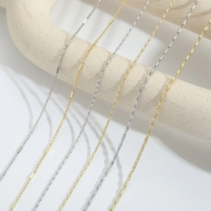 Detailed view of 14k gold plated minimalist chain necklaces on neutral geometric props