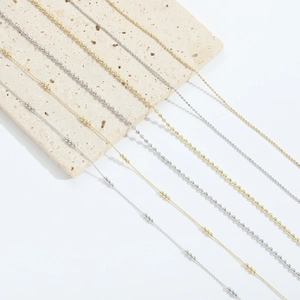 Minimalist 14k gold and silver plated chain necklaces on a beige textured stone base