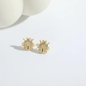 Macro detail of ladybug stud earrings with white zircons and gold plating finish
