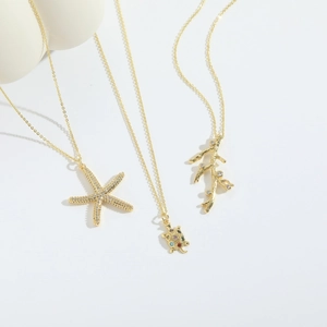 Colliers dorés avec étoile de mer, tortue et corail ornés de zircons sur fond blanc