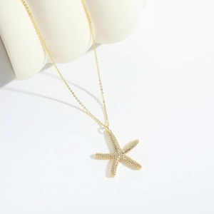 Détail d'un collier pendentif étoile de mer doré orné de zircons sur un support blanc