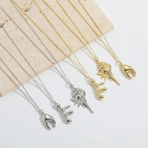 Macro detail of nautical gold and silver necklaces with crab claw and conch shell pendants