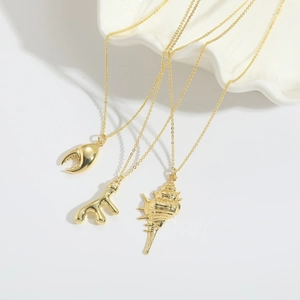 Three gold ocean-themed necklaces featuring crab claw, coral, and conch shell pendants