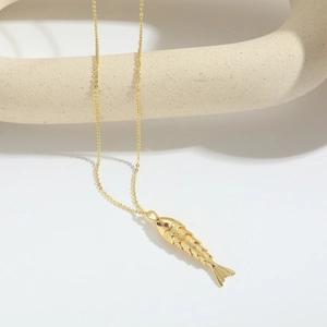 Detailansicht goldener Fisch-Anhänger mit rotem Edelsteinauge und Schuppen auf Stein