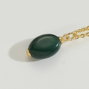 Macro shot of oval dark green gemstone pendant with sleek gold chain necklace