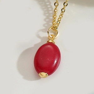Macro detail of a minimalist gold chain featuring a polished red oval stone pendant
