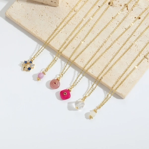 Detail of six minimalist gold necklaces with various colorful gemstone pendants on stone