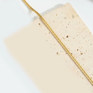 Primer plano de un collar de cadena veneciana dorada minimalista sobre piedra blanca