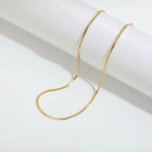 Collar minimalista de cadena box dorada envuelto en un soporte cilíndrico blanco de moda