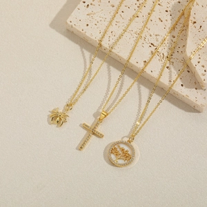 Goldenes Halsketten-Set mit Spinne, Kreuz und Lebensbaum Anhängern auf Steinhintergrund