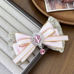 Detail of pink satin bow hair clip with gold edges, silver lace, and teardrop gemstone charm