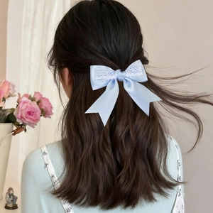 Detail of light blue satin bow hair clip with white lace worn on long wavy hair