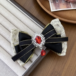 Detail of red gemstone and gold-edged lace bow hair clip on jewelry tray