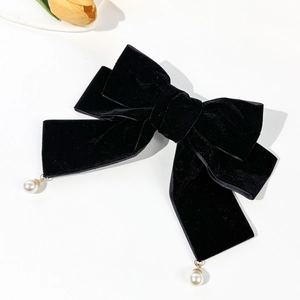Detail view of a black velvet bow hair clip with white pearl pendants on a clean background
