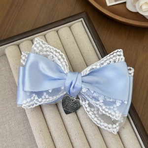 Detail of light blue satin bow hair clip with white lace trim and silver heart pendant