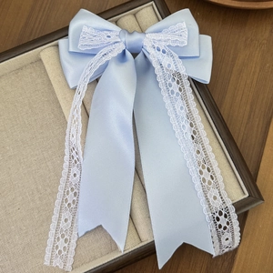 Detail of light blue satin bow hair clip with white lace trim and long ribbons in a box