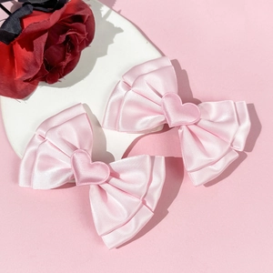 Gros plan de barrettes à nœud en satin rose avec détails de cœur sur plateau blanc