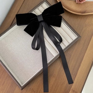 Detail of a large black velvet bow hair clip with long silk streamers on wood base