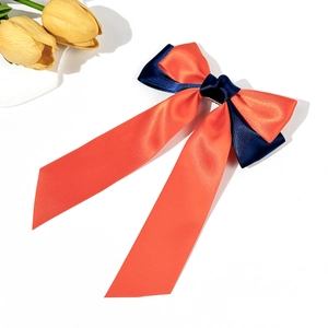 Detailed macro view of orange and navy blue satin bow hairclip with long flowing ribbons
