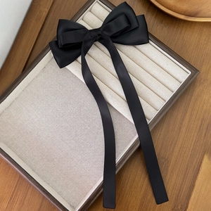 Detail of black satin bow hair clip with long ribbons on a jewelry display tray