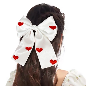 Detail of elegant white satin bow hair clip with red heart appliques worn by a model