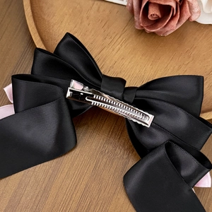 Elegant black satin bow hair clip with pink ribbon on a rustic wooden tray decoration