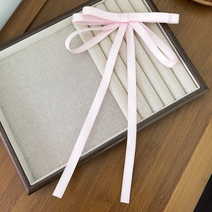 Dettaglio di un fermaglio per capelli a fiocco rosa pallido con lunghi nastri su un vassoio