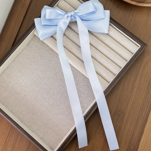 Close-up of light blue satin ribbon bow hair clip with long streamers on a wooden tray