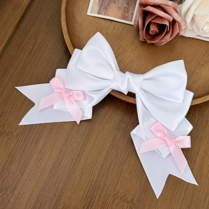 Detailed view of multilayer white satin bow hair clip with pink ribbon accents