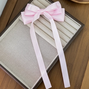 Elegant light pink satin bow hair clip with long ribbons on a jewelry display tray