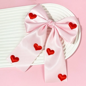 Detail of large pink satin bow hair clip with red heart accents and elegant long ribbons