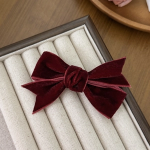 Detail view of the deep red velvet double-layered bow hair clip on a wooden display tray