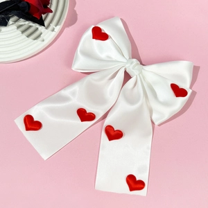 Close-up of white satin bow hair clip with red 3D hearts and long ribbon detail