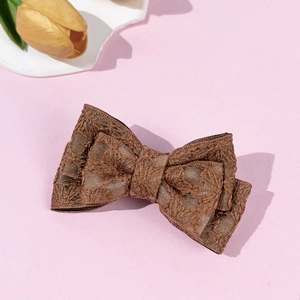 Close-up of brown lace floral bow hair clip on a pink aesthetic background